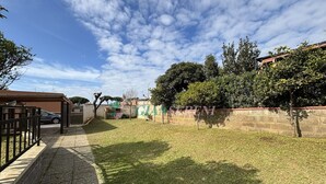 A grassy yard with a stone wall, a metal gate, and a building with a tiled roof. - 5 beds with garden and air conditioning (San Vincenzo)