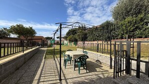 An outdoor patio with a table and chairs, surrounded by a metal fence and greenery. - 5 beds with garden and air conditioning (San Vincenzo)