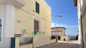 A building with a balcony and a door, a paved street, and a clear sky.