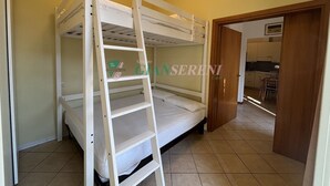 Habitación con literas, una escalera, una puerta de madera que da a una cocina y suelo de baldosas.