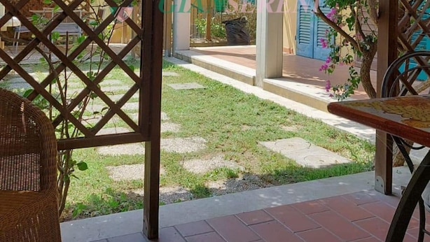 Un espacio al aire libre cubierto con una pérgola de madera, una silla de mimbre y una mesa.