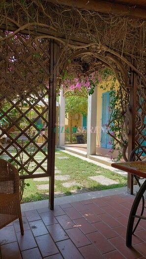 Un espacio al aire libre cubierto con una pérgola de madera, una silla de mimbre y una mesa.