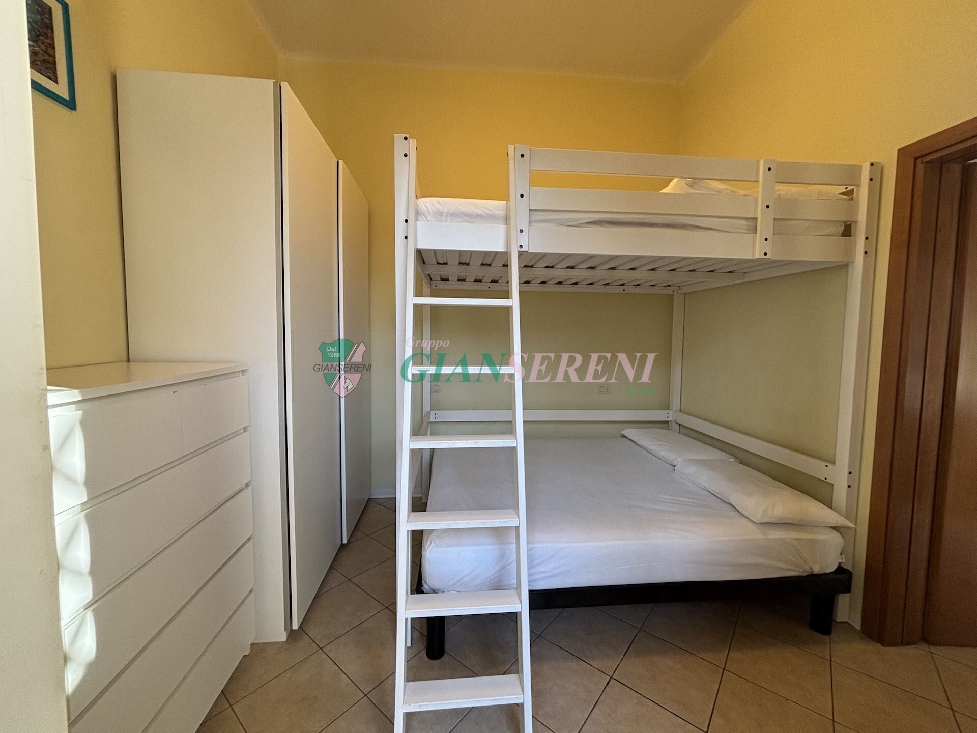 A bunk bed room with a white ladder, a wardrobe, and a door.
