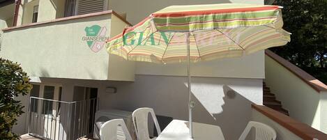 A balcony with a table and chairs, an umbrella, and a building with a logo.