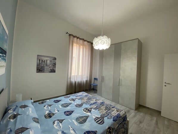A bedroom with a bed, a wardrobe, a chair, and a hanging light fixture.