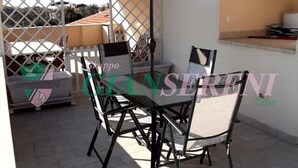 Un patio al aire libre con una mesa, sillas, un paraguas grande y una valla blanca.