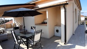 Un pequeño patio al aire libre con mesa y sillas, una lavadora y un paraguas grande.