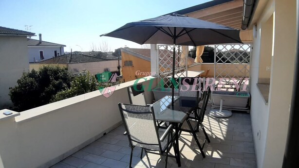 Un balcón con mesa y sillas, un gran parasol y vistas a edificios cercanos.