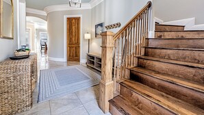 Ein geräumiges Foyer mit einer Holztreppe, einem großen Spiegel und einer Hängeleuchte.
