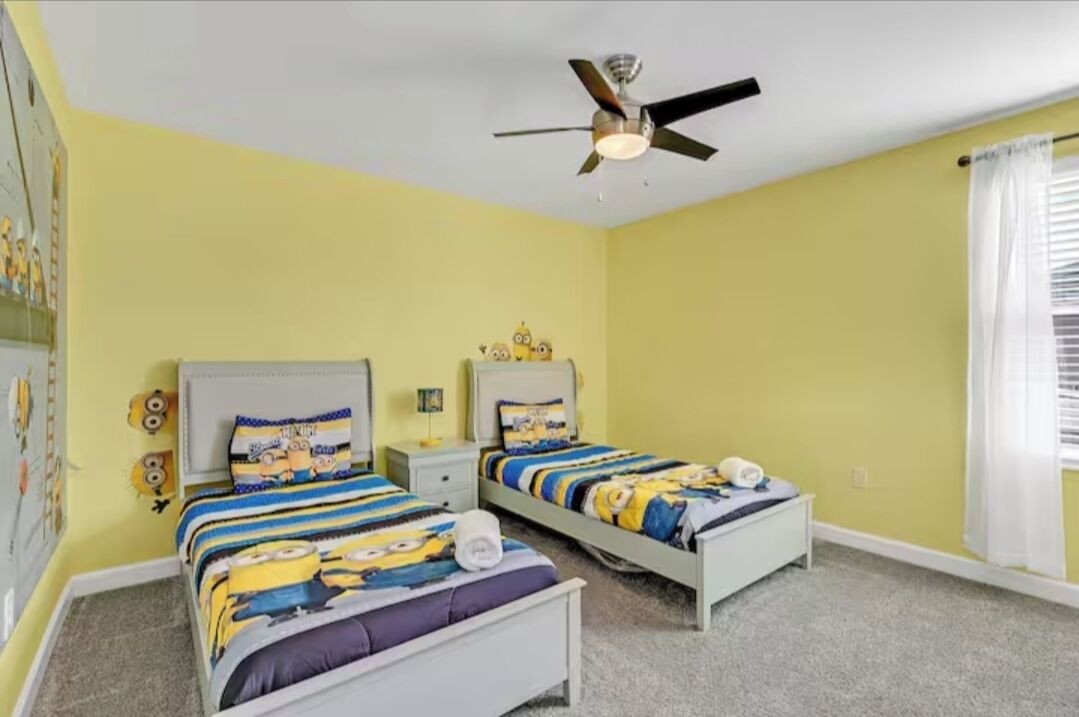 Une chambre avec deux lits, un ventilateur de plafond et une fenêtre avec des rideaux.