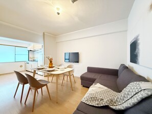 Un salon moderne comprenant un coin repas, un canapé gris et un téléviseur à écran plat fixé au mur.