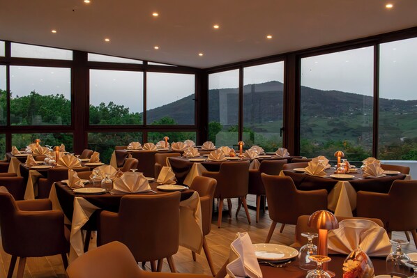 A restaurant with tables set for dining, large windows offering a view of a mountainous landscape.
