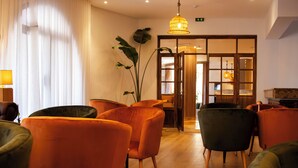 Eine Hotelhalle mit orangefarbenen und grünen Sesseln, Holzboden und einer großen Pflanze.