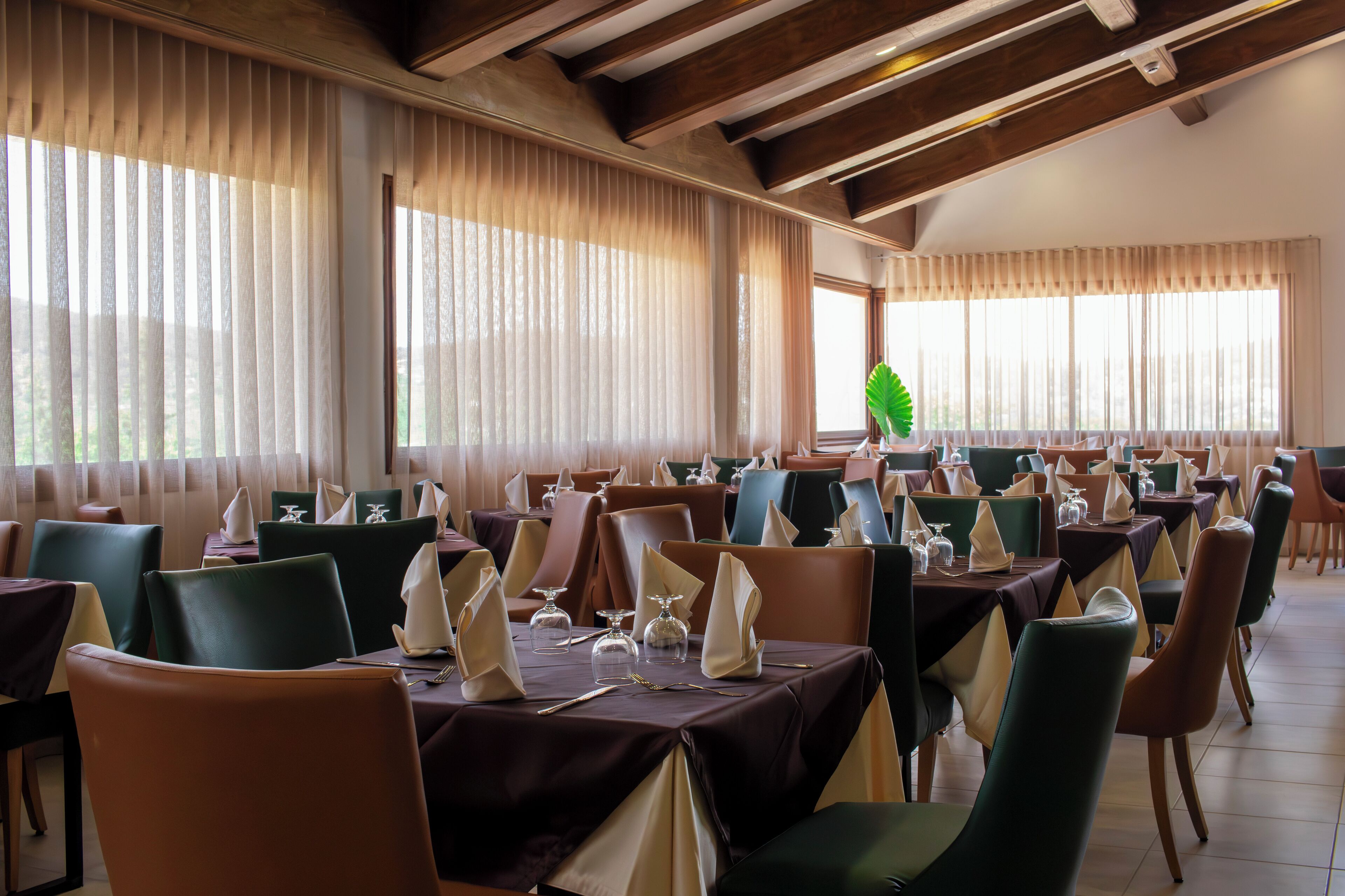 A restaurant with multiple tables set for dining, featuring a variety of chair colors and table settings.