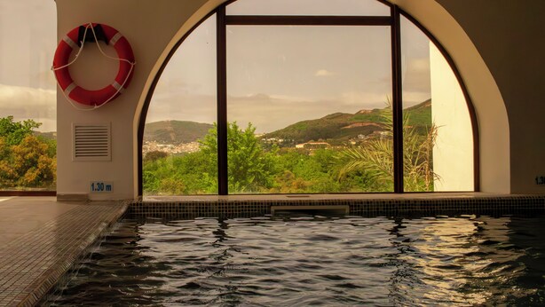 Ein Swimmingpool mit Blick auf eine gebirgige Landschaft durch Rundbogenfenster.