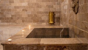Eine freistehende Steinbadewanne mit goldenem Wasserhahn und einer Wandskulptur.