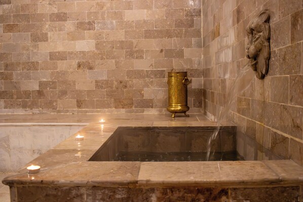 Une baignoire en pierre avec un robinet doré et une sculpture fixée au mur.
