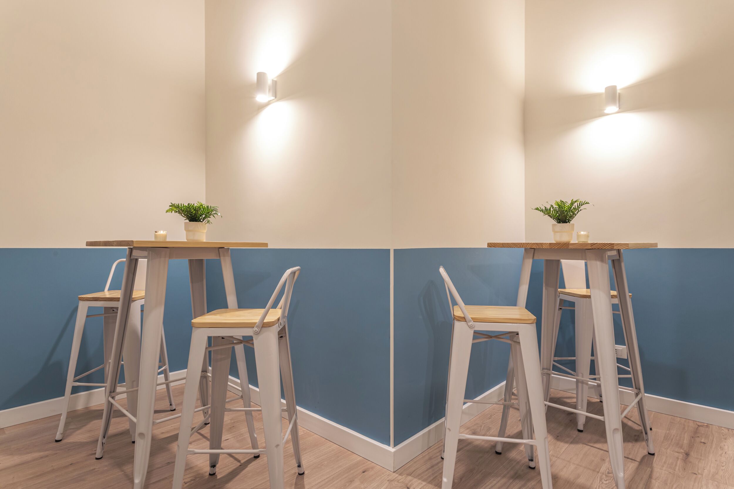 Um canto de um quarto com parede azul, uma mesa de madeira e dois banquetes brancos.