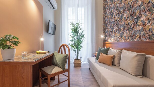 Ein modernes Wohnzimmer mit einem Holztisch, einer bequemen Couch, einer großen Topfpflanze und einem Wand-Fernseher.