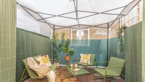 Ein überdachter Patio-Bereich mit grünen Stühlen, einem Tisch mit Kerzen und Blumentöpfen.