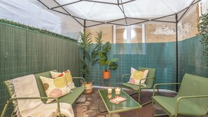 Ein überdachter Patio-Bereich mit grünen Metallmöbeln, einem Tisch mit Kerzen und Topfpflanzen.