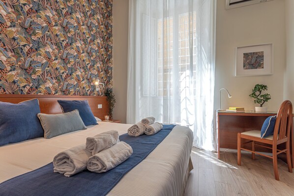 A hotel room with a large bed, a desk, a chair, and a window with curtains.
