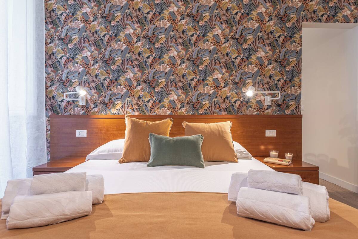 A neatly made bed with white and brown bedding, a patterned wall behind, and two bedside tables with candles.