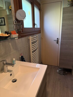 Moderni kylpyhuone, jossa on valkoinen pesuallas, peili, pyyhekoukku ja ovi.