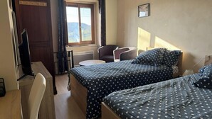 A room with two beds, a desk, a chair, a window with curtains, and a picture on the wall.