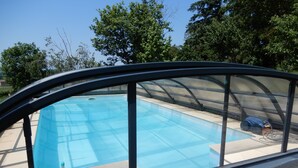 A swimming pool with a clear blue water surface, surrounded by a covered area with a curved roof.