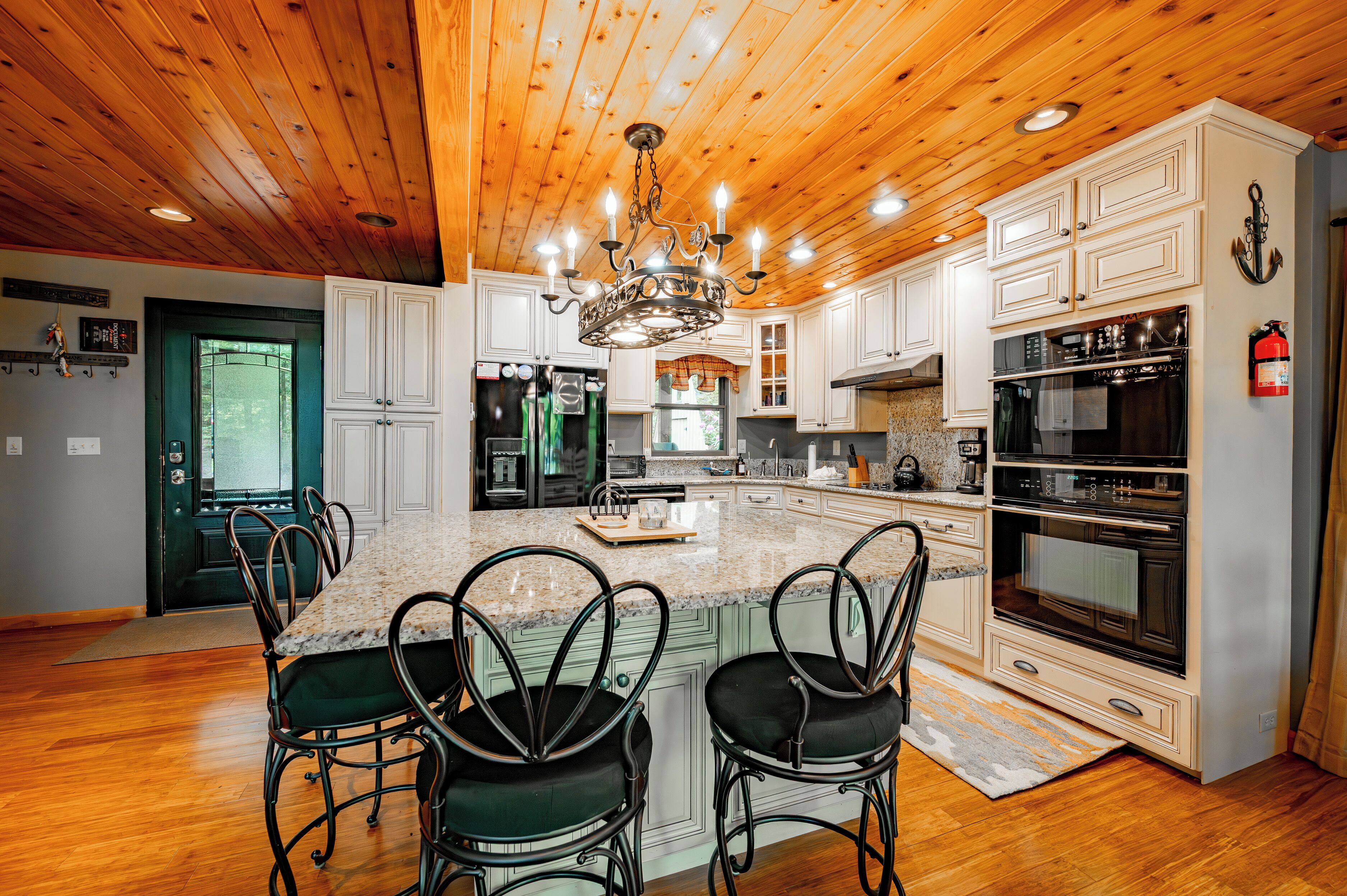 A kitchen with wooden ceiling, white cabinets, a central island with chairs, and stainless steel appliances.