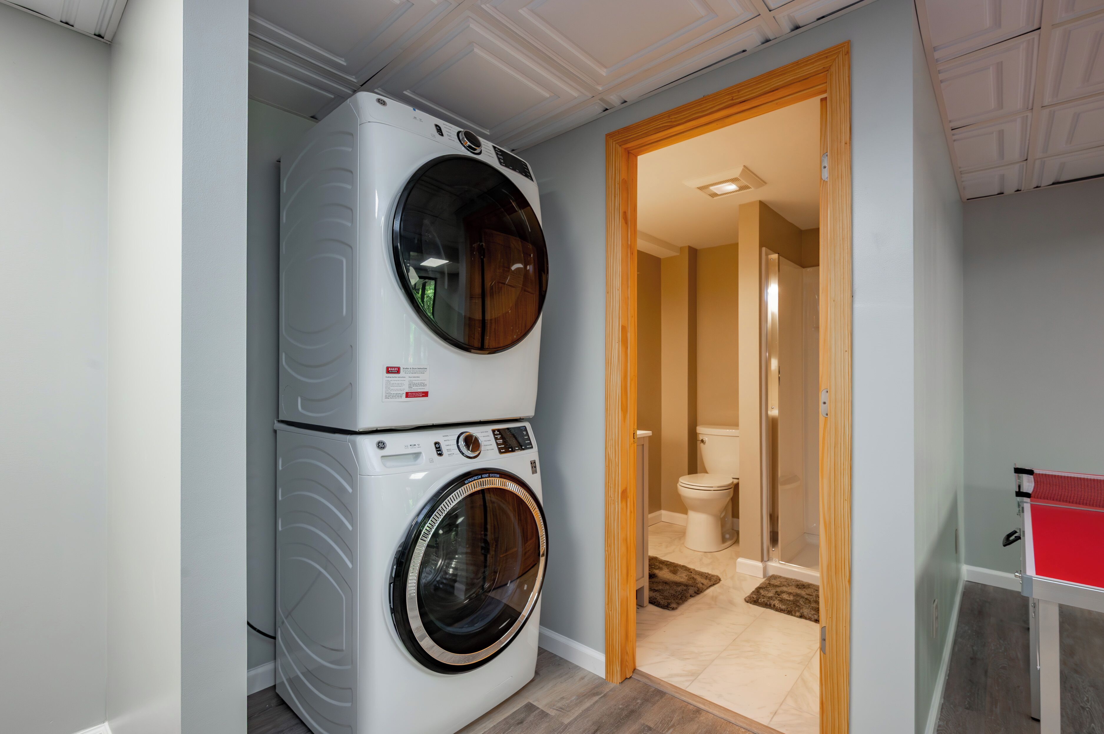 Une buanderie équipée d’une machine à laver et d’un sèche-linge superposés, de toilettes et d’une table de ping-pong.