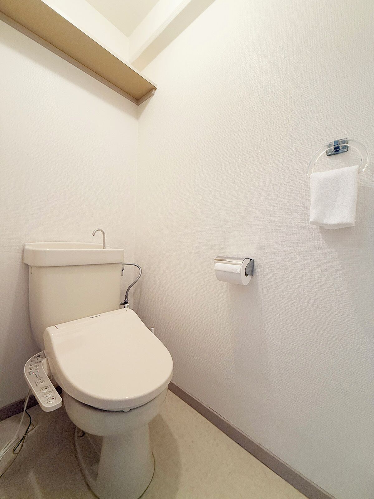 A standard white toilet with a foot pedal, a toilet paper holder, and a towel rack on the wall.