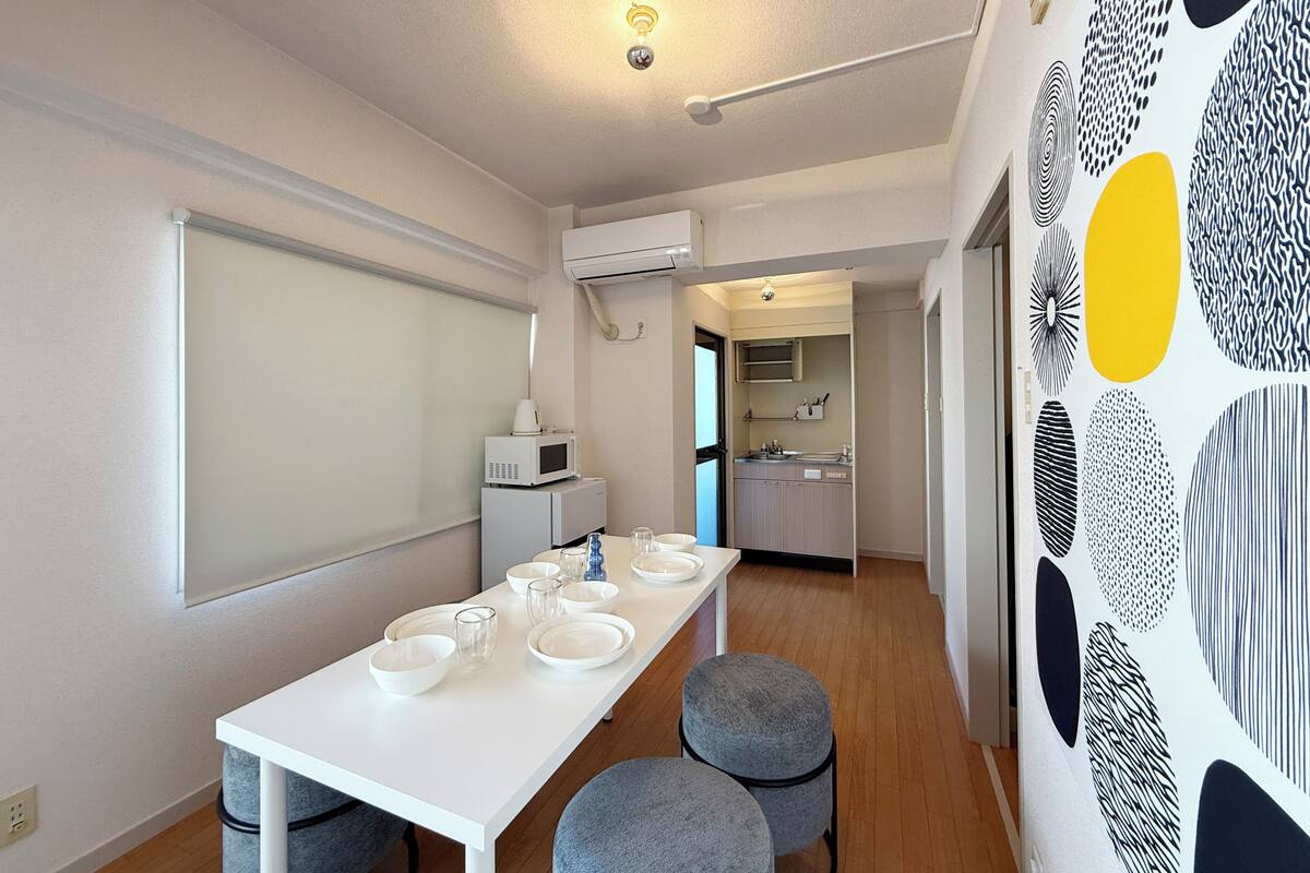 A modern kitchen with a microwave, sink, and cabinets. There is a dining area with a white table and grey chairs.