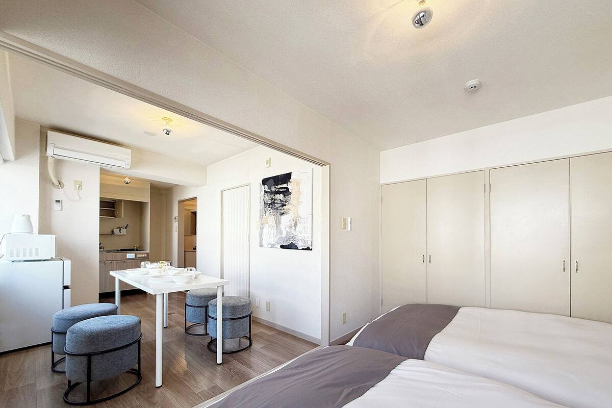 A modern hotel room with a bed, a desk, and a kitchenette.