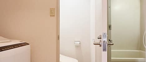 A compact bathroom with a toilet, a shower area, and a washing machine.