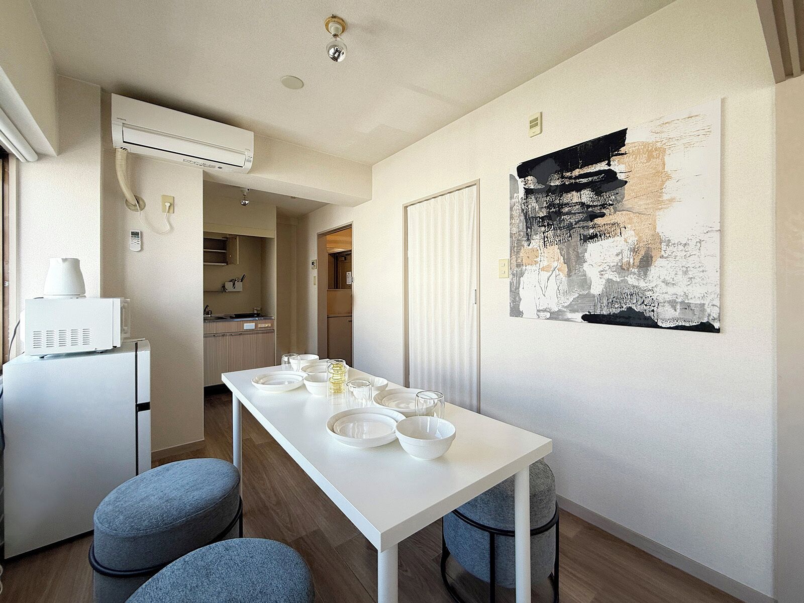 Una cocina moderna con electrodomésticos blancos, una mesa de comedor dispuesta con cuencos y vasos, y un cuadro abstracto de gran tamaño en la pared.