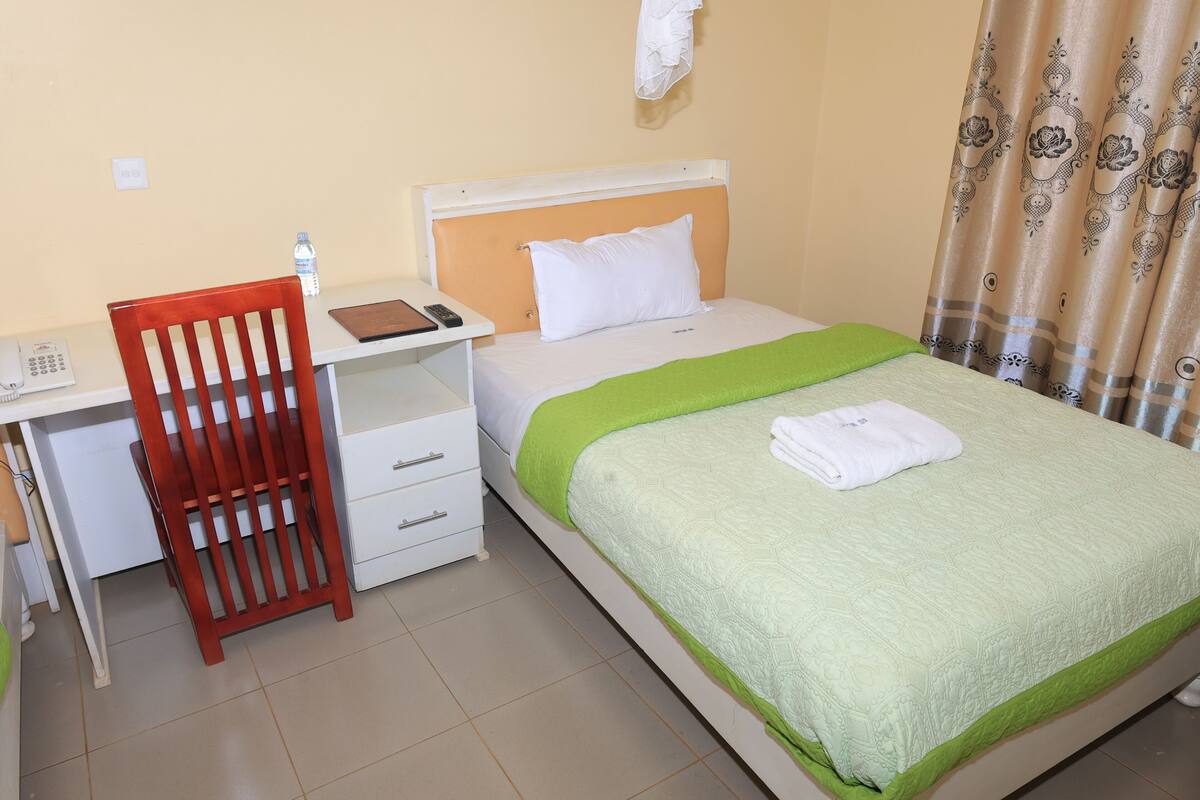 A hotel room with a bed, a desk, a chair, a water bottle, and a telephone.