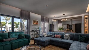 Ein modernes Wohnzimmer mit Ecksofa, Couchtisch und großen Fenstern mit Vorhängen.