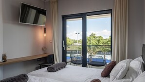 Ein Hotelzimmer mit Bett, Wandfernseher, Schreibtisch mit Stuhl und Balkon mit Sitzgelegenheit.