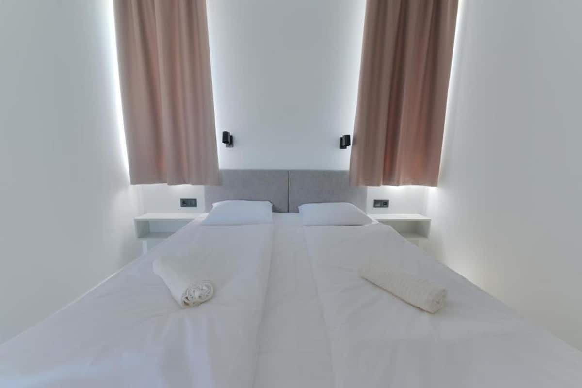Un lit double avec du linge de lit blanc, deux tables de chevet et une tête de lit.