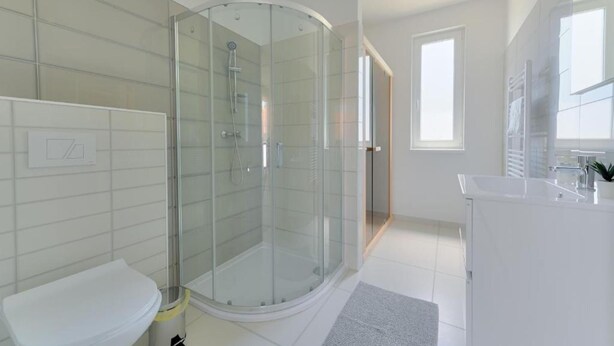 Ein modernes Badezimmer mit einer gläsernen Duschkabine, einem weißen Waschbecken und einem großen Fenster, das für natürliches Licht sorgt.