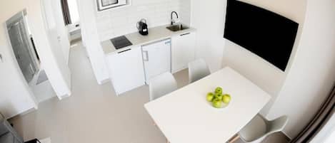 A compact kitchen with white cabinets, a microwave, and a sink. There is a dining table with four chairs and a bowl of fruit.