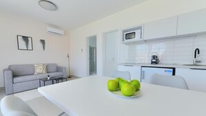 Een moderne keuken met witte kasten, een magnetron en een koffieapparaat. Er staat een eettafel met een bord groene appels.