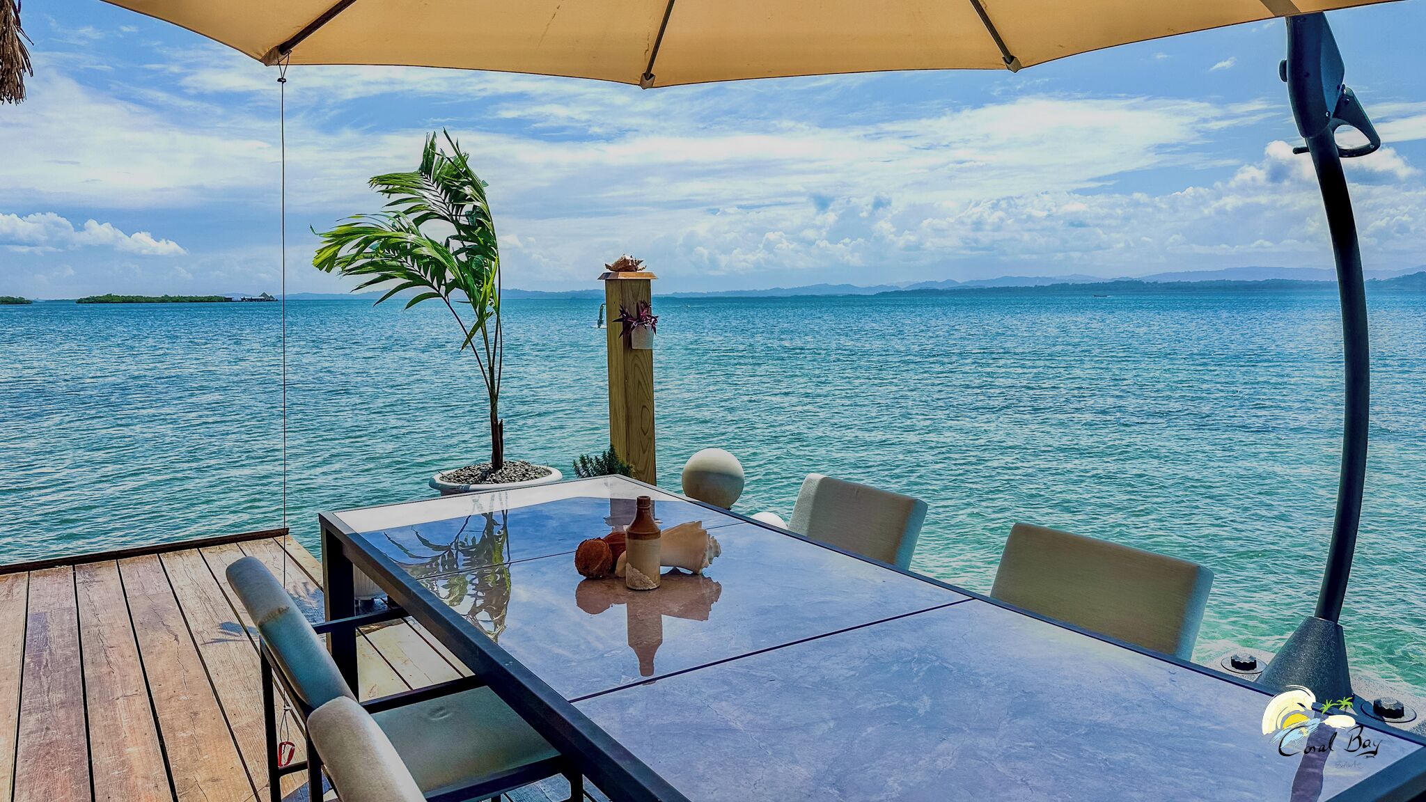 A table with chairs and a glass top, overlooking a body of water with a clear sky.