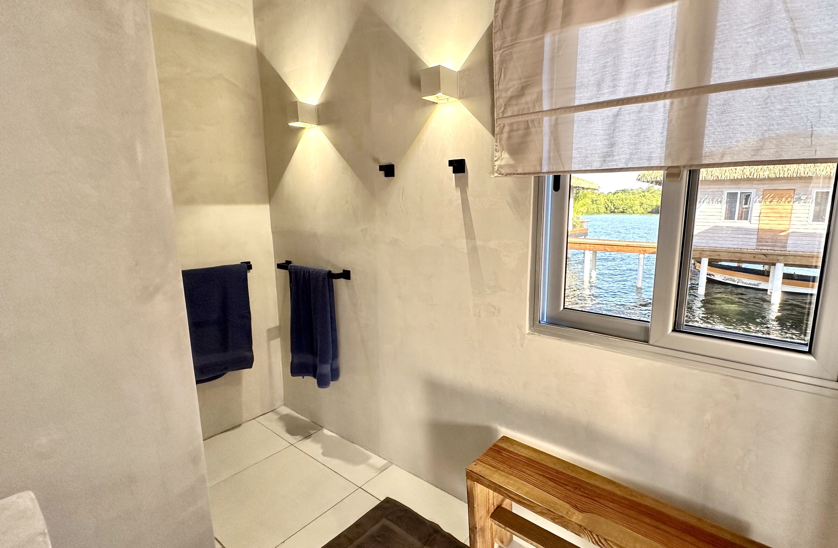 Un baño con un ventanal grande, un banco de madera y dos toallas colgadas en la pared.