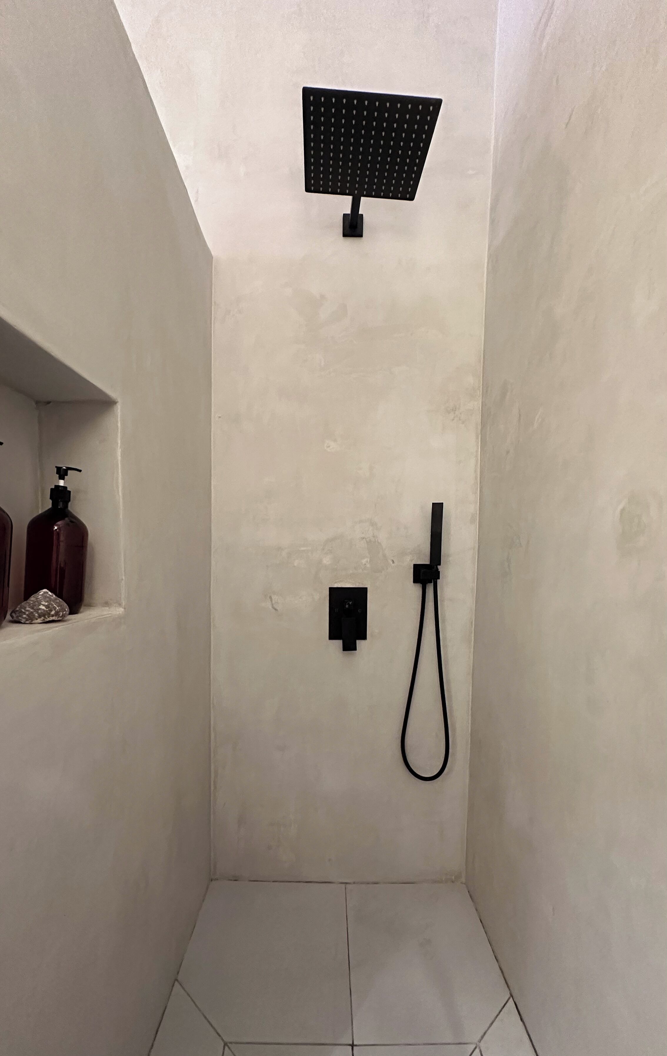 A small, tiled shower room with a black showerhead and a handheld shower attachment.