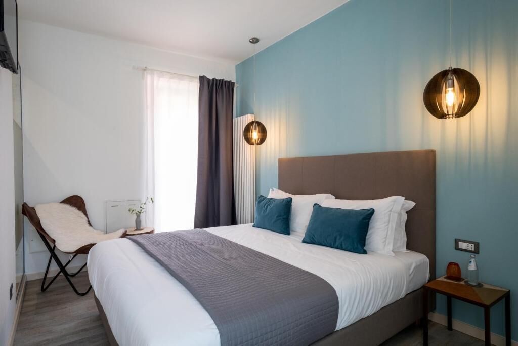Une chambre d’hôtel avec un grand lit, une chaise, une table de chevet et un luminaire fixé au mur.