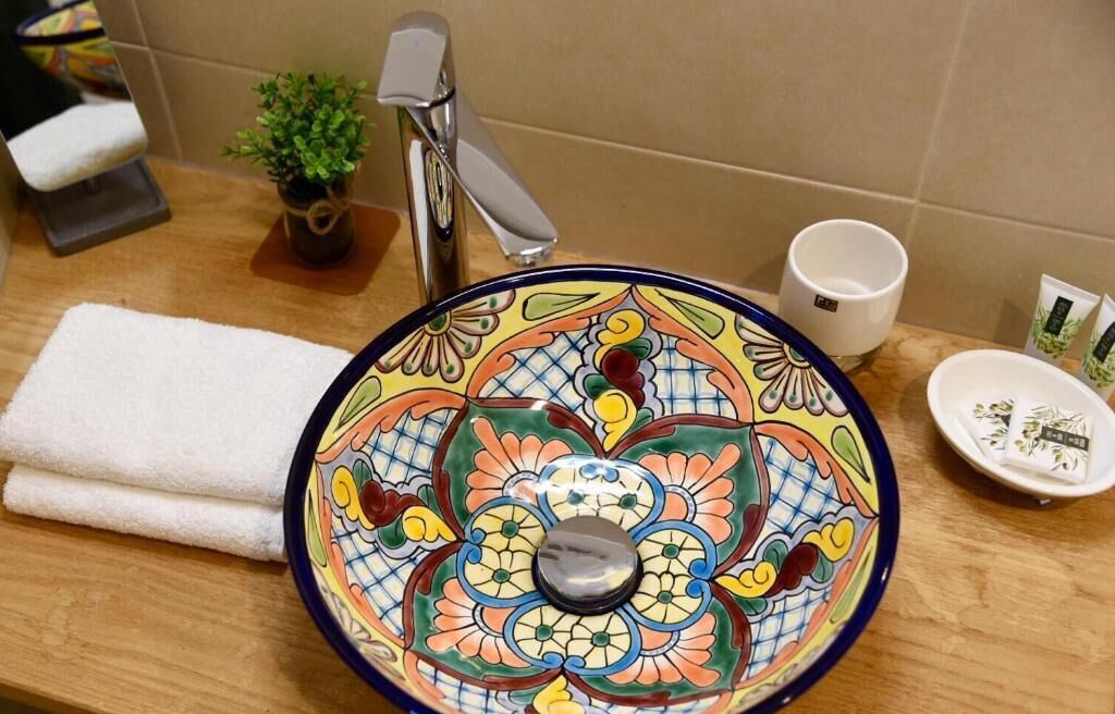 A bathroom with a colorful ceramic sink, a small potted plant, a white towel, and a cup on the counter.