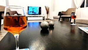 Una sala de estar con televisor, un vaso de líquido color ámbar y una vela sobre una mesa negra.
